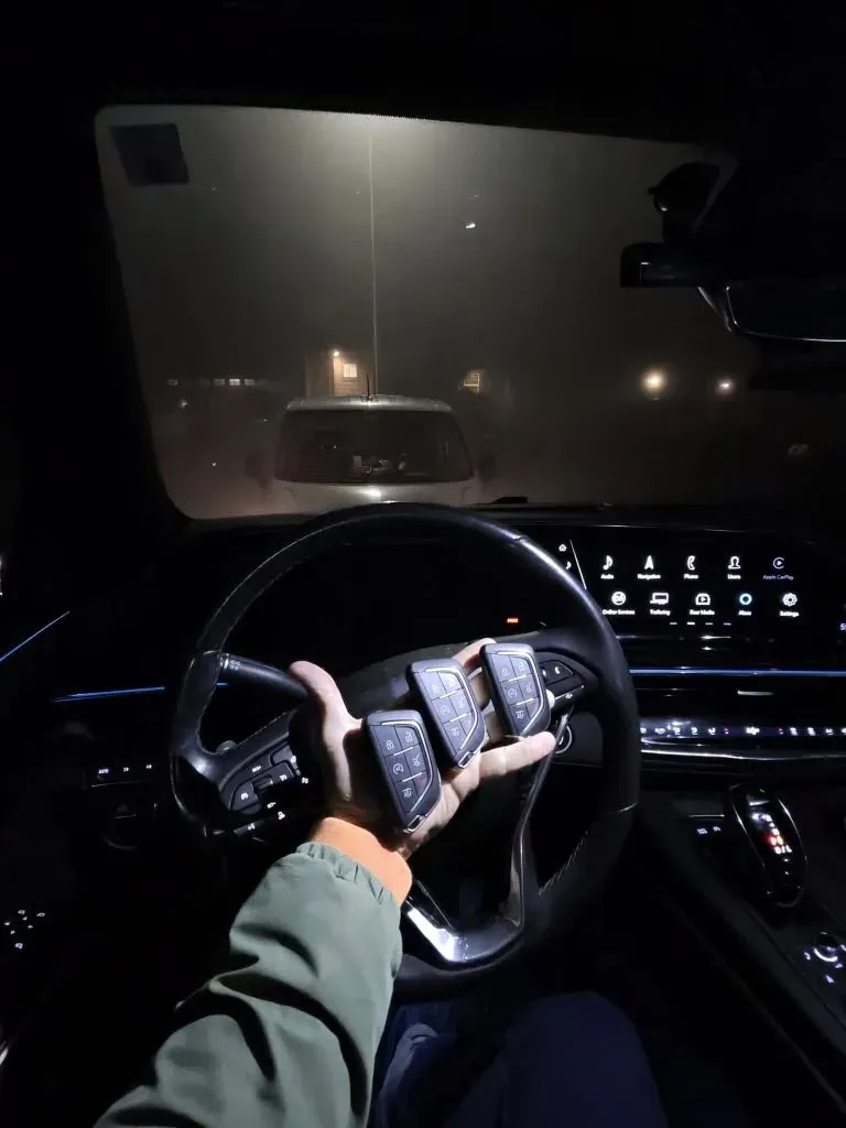 Hand holding three new smart keys at the steering wheel of a car at night
