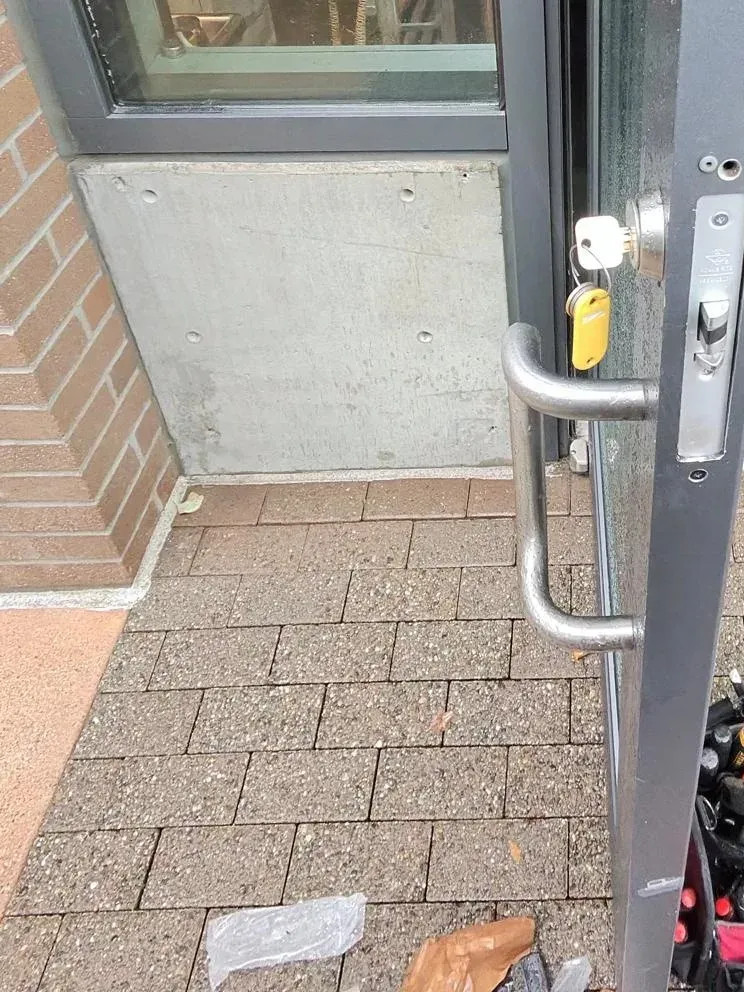 Tool bag on the sidewalk at an open business door with a key in the lock